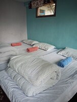 A double bed with white bedding and polka dot pillows, a teal wall, and a window with a patterned curtain.