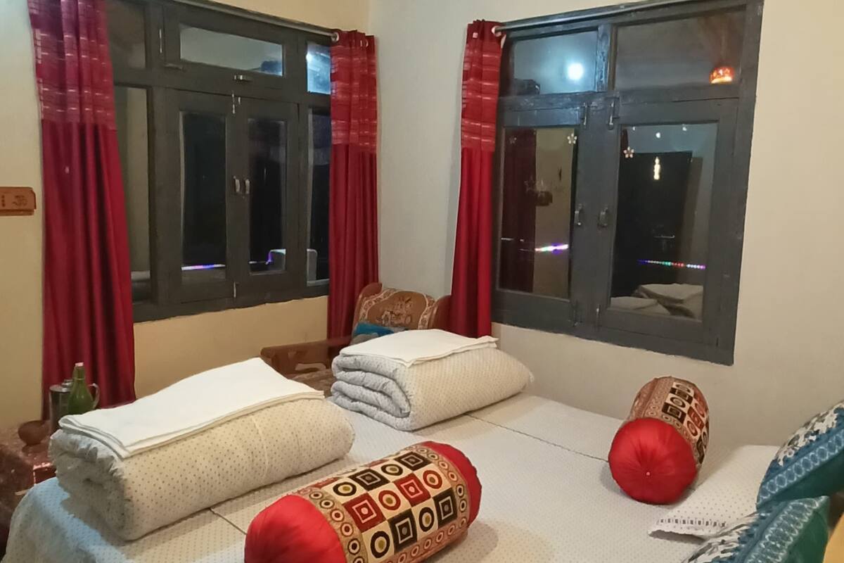 A bedroom with a wooden ceiling, a bed with white bedding and red pillows, and two windows with red curtains.