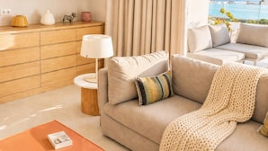 A modern living room with a sofa, a coffee table, a lamp, and a view of the ocean.