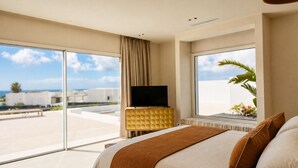 A hotel room with a large bed, a TV on a wooden stand, and a balcony with a view of the city.