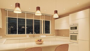 A modern kitchen with a large window, pendant lights, a central island with chairs, and built-in appliances.