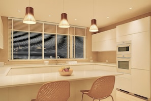 Una cocina moderna con un ventanal grande, lámparas colgantes, una isla central con sillas y electrodomésticos integrados.