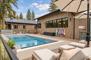 Un espace piscine avec des chaises longues, un bâtiment en bois doté de grandes fenêtres et un présentoir à drapeaux.
