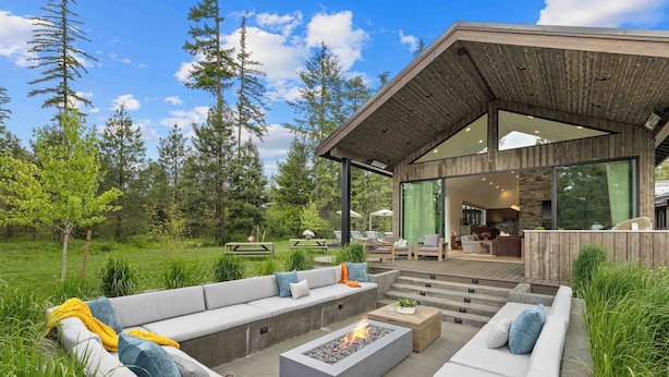 Un espace de vie extérieur moderne, doté d’un foyer, de sièges et d’une terrasse en bois.