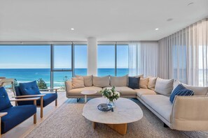 A modern living room with a large sofa, two armchairs, and a coffee table. The room has large windows offering a view of the ocean. - Dali by Khove (Burleigh Heads)