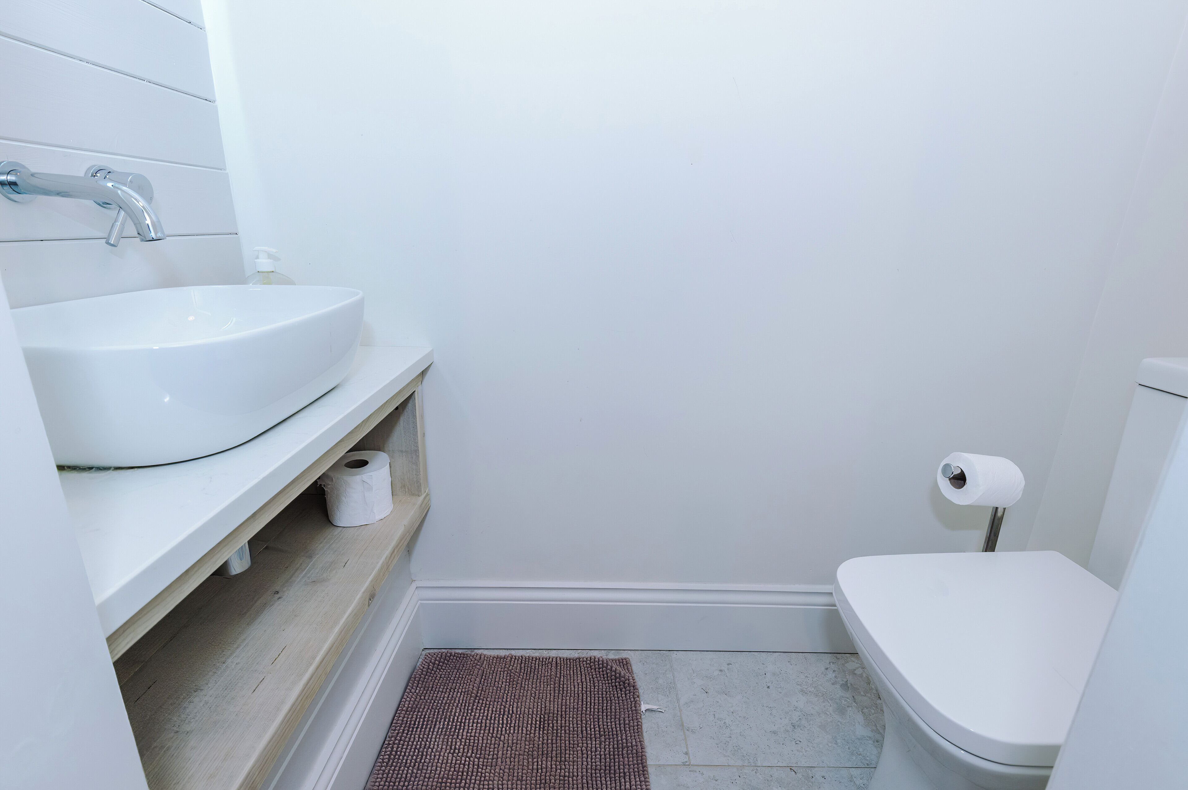 Et lille, rent badeværelse med en hvid vask, toilet og en rulle toiletpapir.