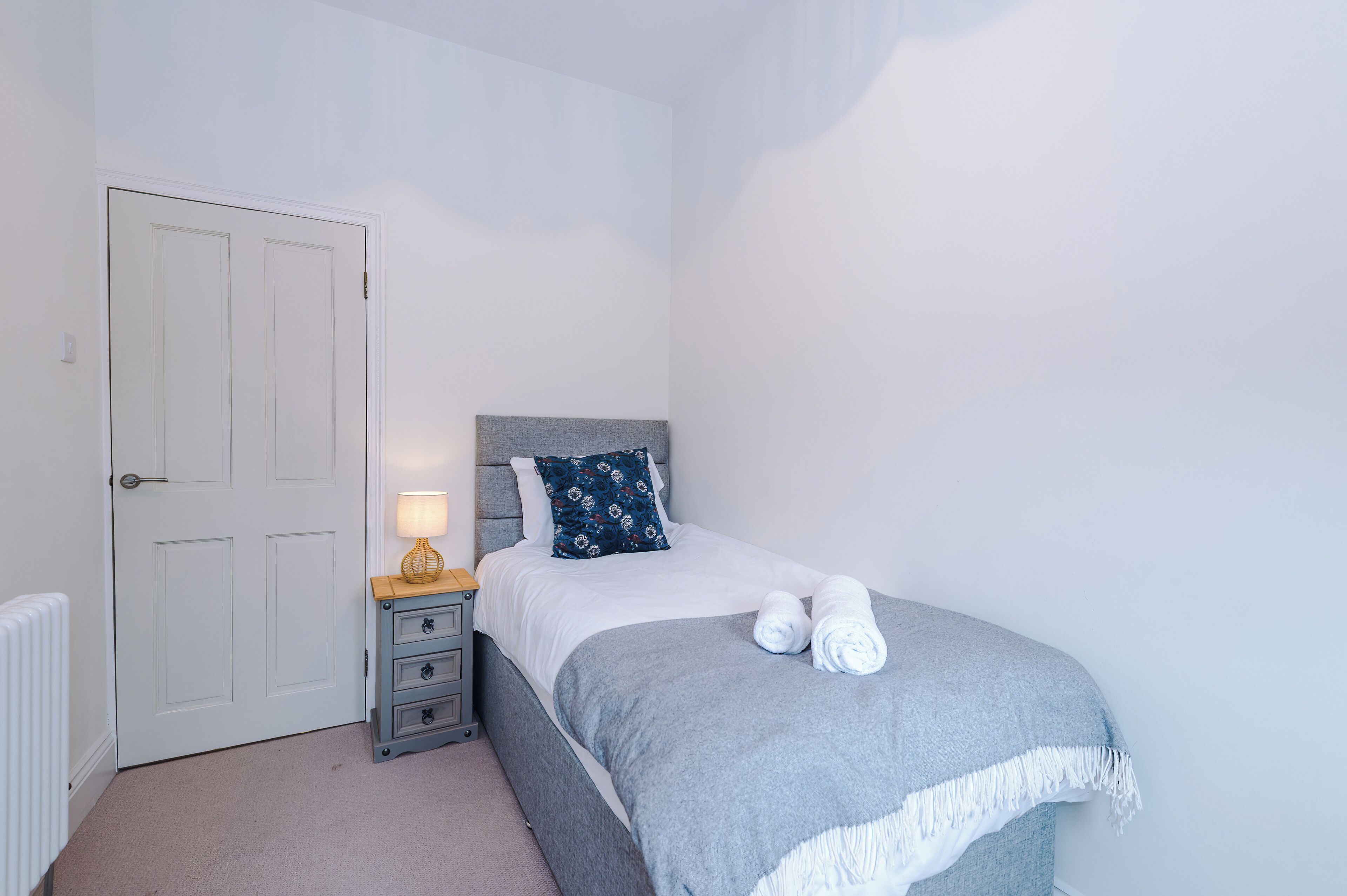 A bedroom with a bed, a nightstand, a lamp, and a door.