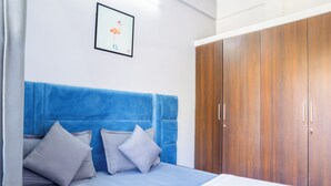 A bedroom with a blue headboard, two pillows, a wooden wardrobe, and a framed picture on the wall. - Housr Marathahalli Near Bagmane Park (Bengaluru)