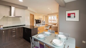 Una cocina moderna con armarios de madera oscura, extractor de acero inoxidable y comedor con mesa de vidrio para cuatro comensales.