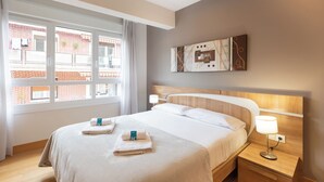 Habitación de hotel con una cama grande, dos mesitas de noche, un ventanal con vista a un edificio de ladrillo y una obra de arte colgada en la pared.
