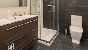 Un baño moderno con ducha envuelta en vidrio, un lavabo blanco con espejo y una pared revestida de baldosas oscuras.