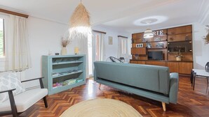 Un salón con sofá, una estantería, una mesa de comedor y una cocina con armarios y televisión.