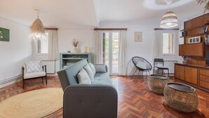 Una sala de estar con un sofá, sillas, un televisor y una estantería.