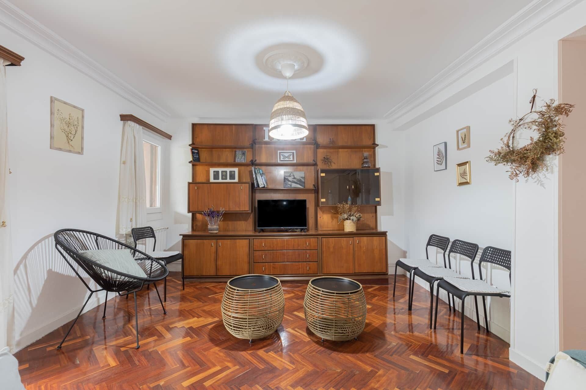 Ein Zimmer mit Holzschrank, Fernseher, Korbstühlen und Deckenleuchte.