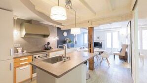 Een moderne keuken met een centraal eiland, een eethoek met een ronde tafel, en een woonruimte met een televisie en zitplaatsen.