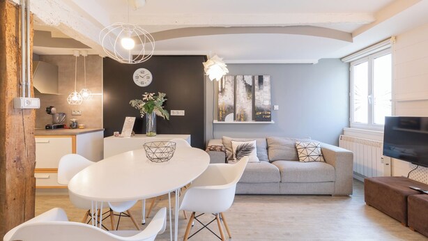 Een moderne woonkamer met een grijze bank, een eettafel met stoelen en een televisie.