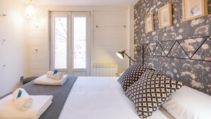 Hotelkamer met een bed, twee nachtkastjes, een bureau, een stoel, een bureaulamp, een wandplank en een raam met jaloezieën.