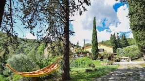 A hammock in a lush garden with a stone pathway leading to a yellow house surrounded by greenery and trees. - Amazing home in Cortona (Cortona)