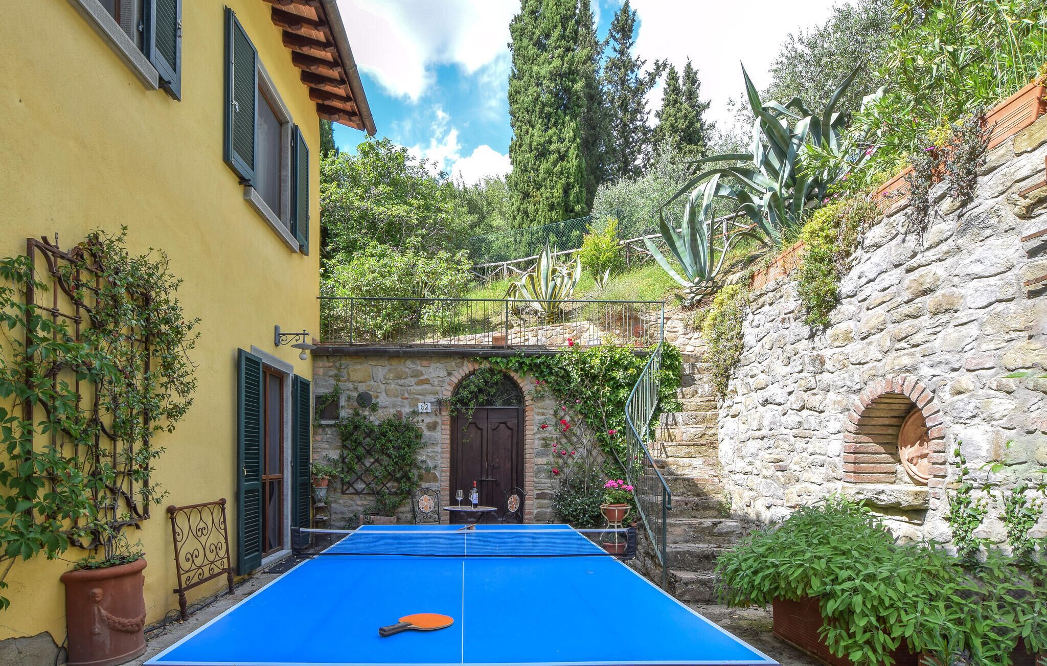 Un patio con mesa de ping pong, un muro de piedra y un edificio amarillo con contraventanas.