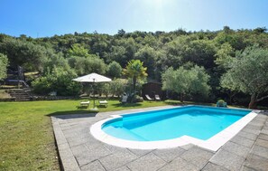 Une piscine dotée d’une plage en pierre, entourée d’une pelouse verdoyante et d’arbres.