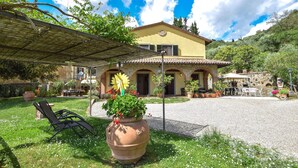 A yellow villa with a stone facade, a covered patio with outdoor furniture, and a large flower pot in the foreground. - Amazing home in Cortona (Cortona)
