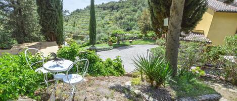 Un patio con mesa y sillas redondas, rodeado de vegetación y vistas a una colina.
