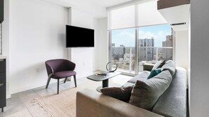 A modern living room with a large window, a flat-screen TV, a purple chair, and a grey sofa.