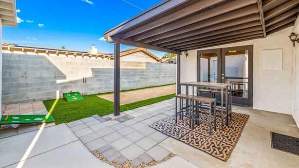 A patio area with a table and chairs, a small lawn, and a wall with a window. - 1 BR Large Desert ADU Retreat with Bocce Court (Bermuda Dunes)