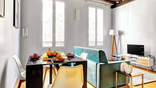 Un salon moderne avec un coin repas, comprenant un canapé, un téléviseur et une table à manger dressée pour le petit-déjeuner.