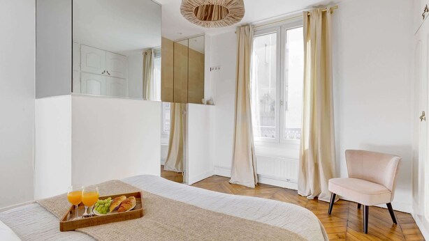 Habitación de hotel con cama, bandeja de desayuno con croissants y jugo, una silla y un espejo grande.