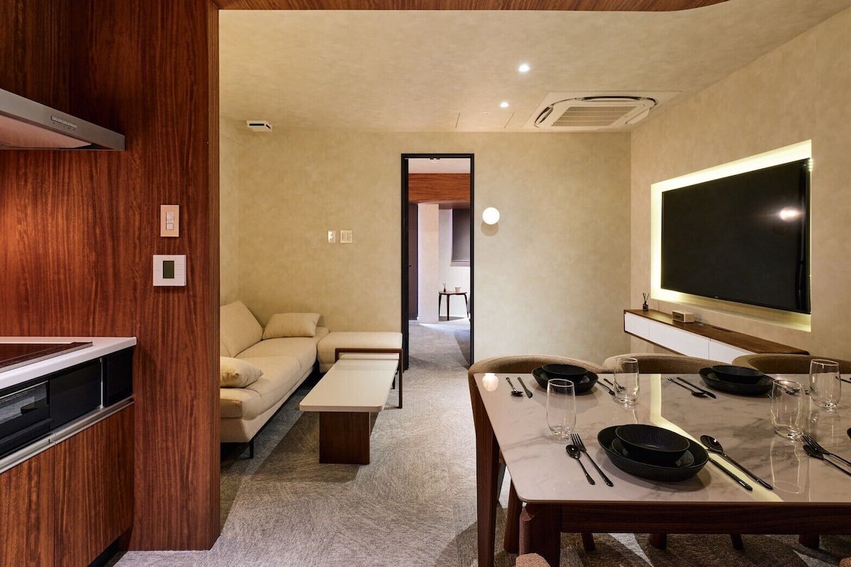 Una sala de estar moderna con un sofá, una mesa de comedor para dos personas y un televisor de pantalla plana grande montado en la pared.