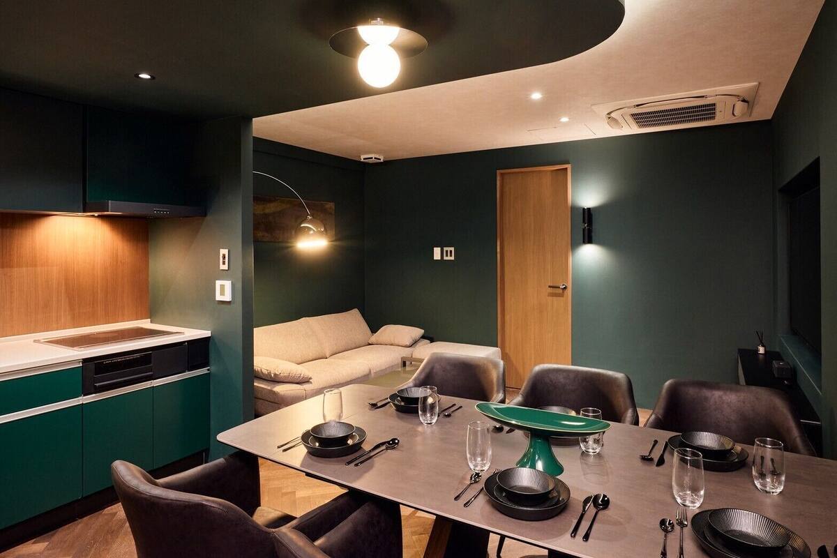 Un comedor moderno con una mesa de madera dispuesta para cuatro personas, un sofá y una cocina con horno empotrado.