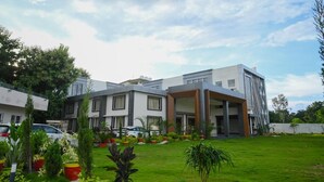 A modern building with a flat roof, large windows, and a covered entrance. There are potted plants and a well-maintained lawn in front. - Jai Vilas Palace & Resort (Pali)