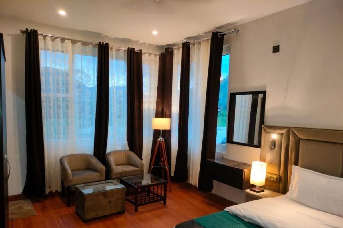 A hotel room with a bed, two armchairs, a small table, a desk, and a lamp.