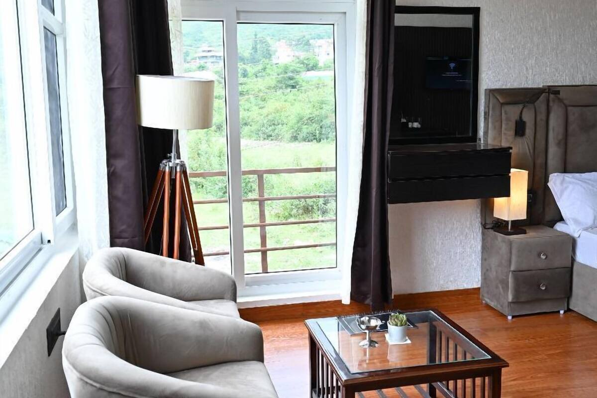 A modern living room with a sofa, a glass coffee table, a TV mounted on the wall, and a balcony with curtains.