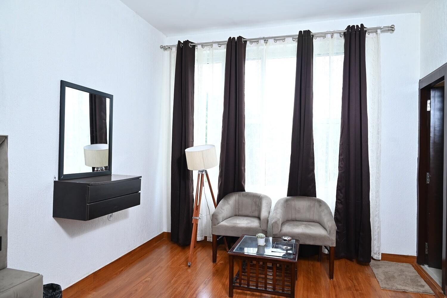 A room with a black console table, two armchairs, a floor lamp, a small table with a plant, and a large window with curtains.