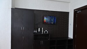 Una habitación con un armario de madera oscura, un televisor de pantalla plana montado en la pared y un estante pequeño con una tetera y otros objetos.