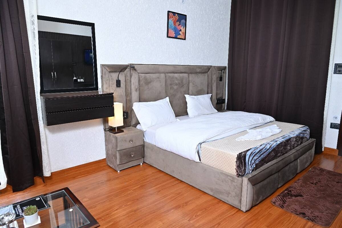 A bedroom with a bed, a bedside table, a mirror, a wall-mounted TV, and a small potted plant.