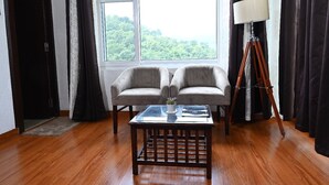 Una habitación con un gran ventanal, dos sillones, una mesita y una lámpara de pie.