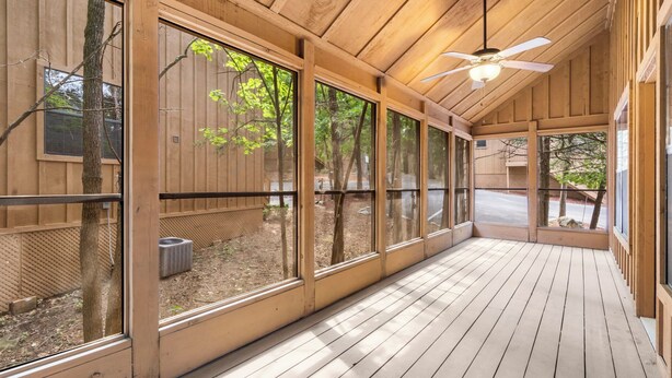 Eine überdachte Holzterrasse mit großen Fenstern, einem Deckenventilator und Blick ins Freie.
