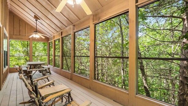 Une terrasse en bois avec des tables de pique-nique et de grandes fenêtres donnant sur une forêt.