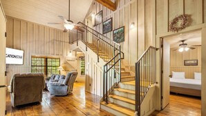 Un salon spacieux doté d’un plancher en bois, d’un escalier avec une rampe en métal et d’une grande fenêtre laissant entrer la lumière naturelle.