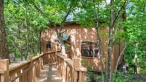 Une cabane en bois dotée d’une terrasse en bois et d’une rambarde en métal, entourée d’arbres.