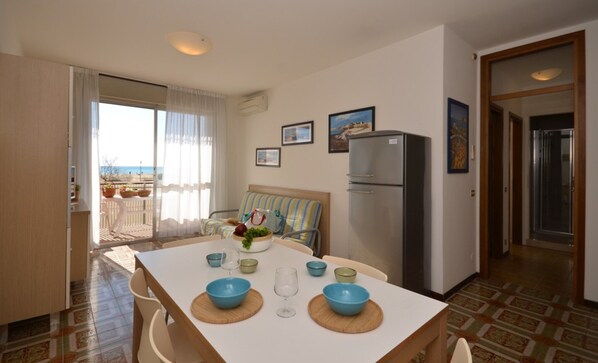 A compact hotel room with a balcony, a dining table set with blue bowls and a wine glass, and a refrigerator. - Sunny beachfront home (Bibione)