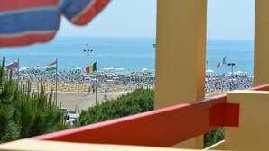 Ein Strand mit mehreren Reihen Sonnenliegen und Sonnenschirmen, Flaggen und freiem Blick auf das Meer.
