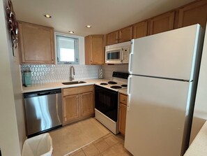 Una cocina con armarios de madera, lavavajillas de acero inoxidable, refrigerador blanco, microondas y estufa.