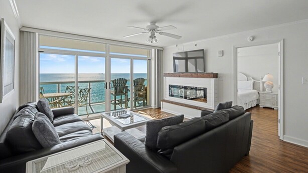 A spacious living room with a large sliding glass door leading to a balcony with a view of the ocean. There is a fireplace with a TV above it, and a cozy seating area with a coffee table. - Enjoy a memorable beach vacation! | Laguna Keyes -  903 (North Myrtle Beach)