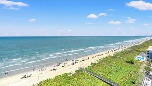 A beach with a long stretch of sand, a wooden fence, and a building with a pool. - Enjoy a memorable beach vacation! | Laguna Keyes -  903 (North Myrtle Beach)
