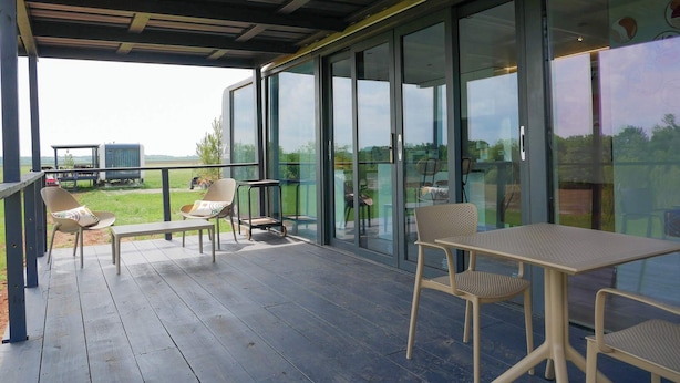 A covered outdoor area with a wooden deck, glass sliding doors, and outdoor furniture including chairs and a table. - Rustic Ranch and the Vessels of tomorrow (Satin)