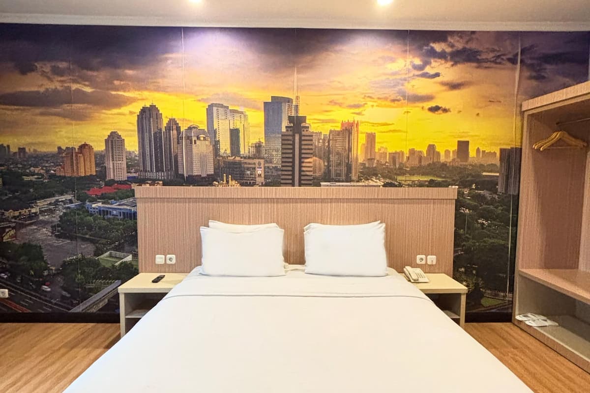 A hotel room with a large bed, two bedside tables, and a cityscape mural on the wall.